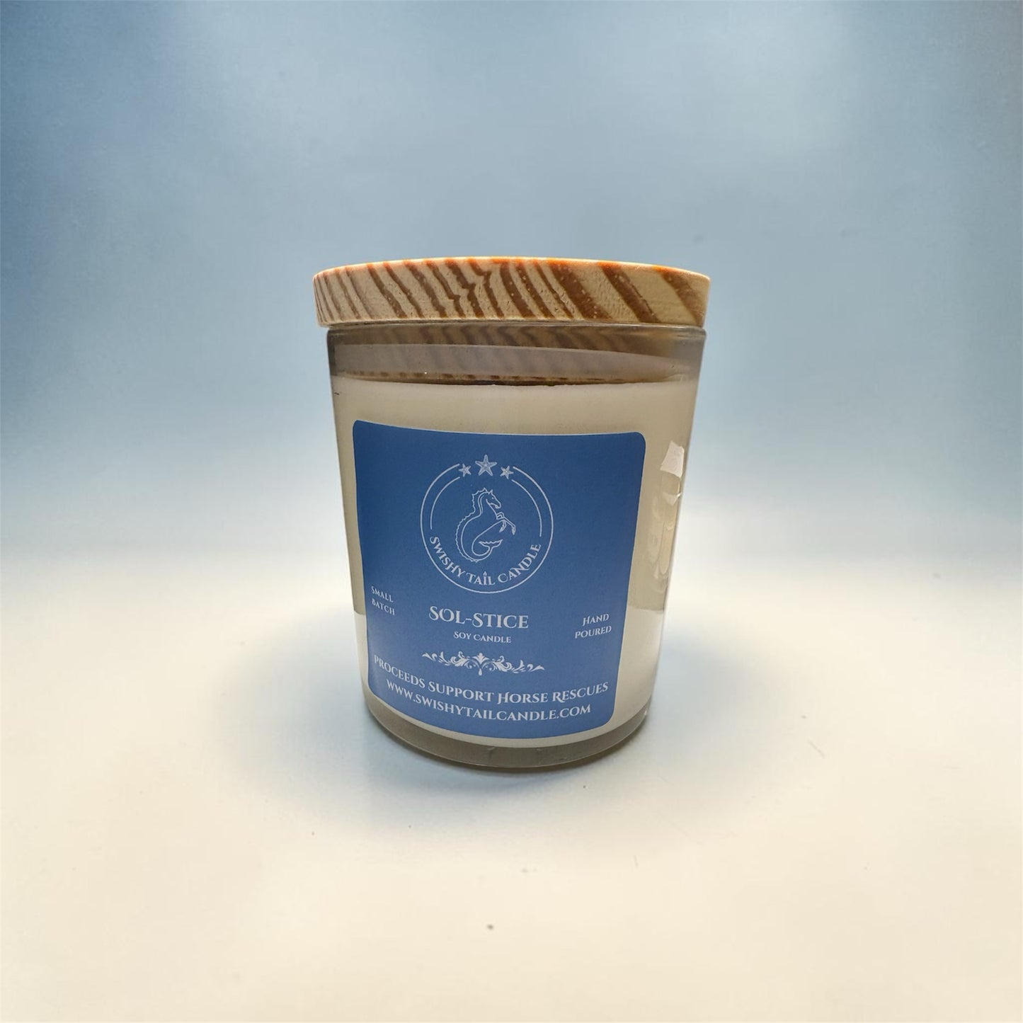 Swishy Tail Candle Sol-Stice soy wax candle in a glass jar with a rustic natural wood lid and blue label.